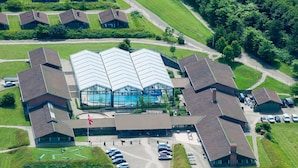 An aerial view of a building complex with a central swimming pool, surrounded by multiple smaller buildings, a parking area, and green lawns. - 6 Person Holiday Home on a Holiday Park in Hanstholm (Hanstholm)