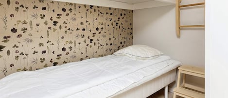 A single bed with a floral-patterned headboard in a small, well-lit room with a wooden floor.