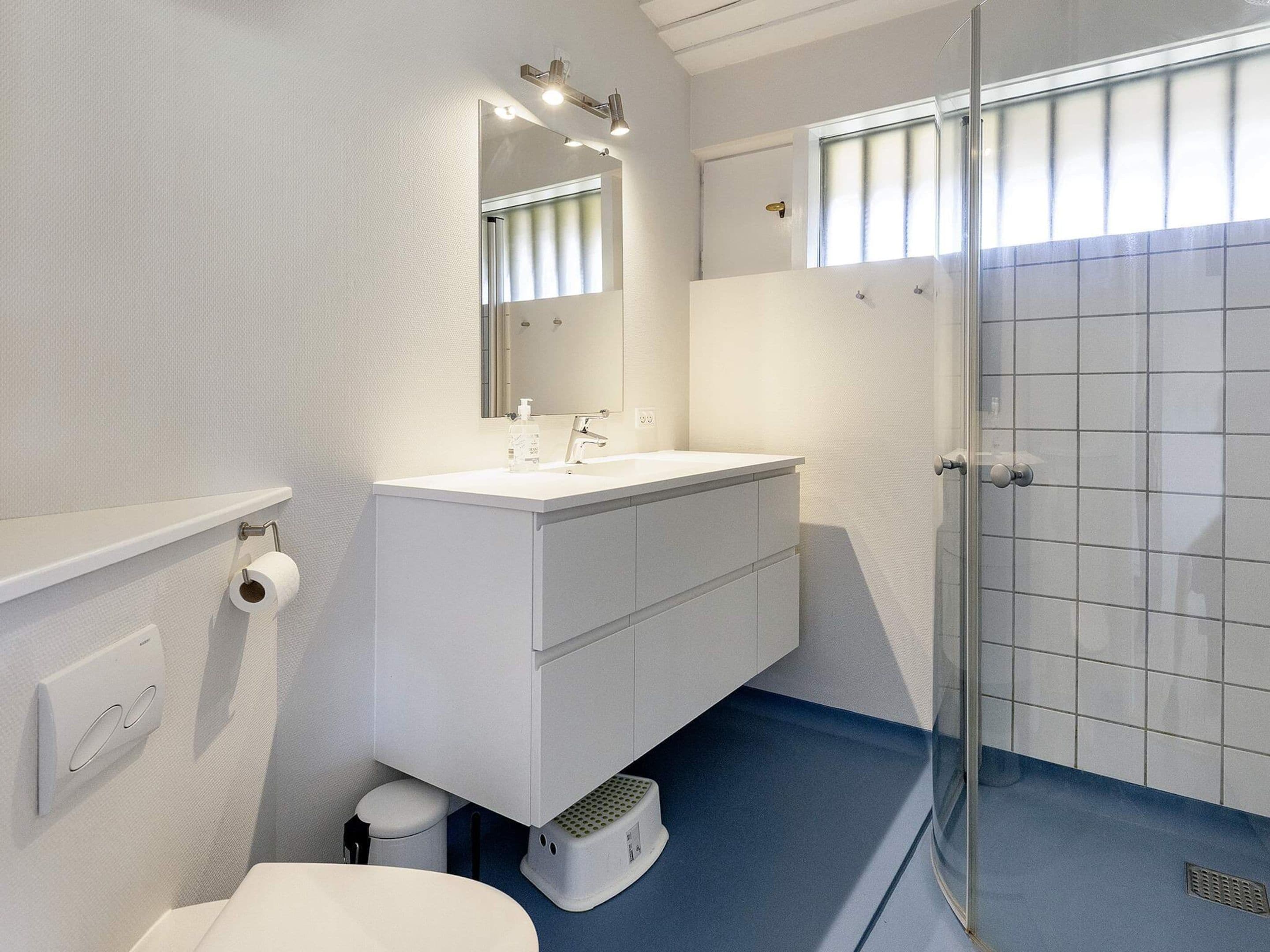 A modern bathroom with a white vanity, a large mirror, a glass shower enclosure, and a blue floor.