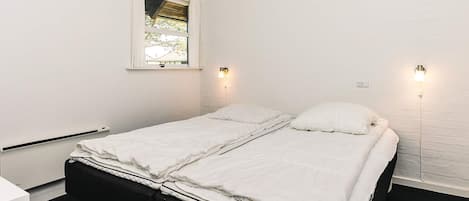 A single-bed room with white bedding, a window, and two wall-mounted lights.