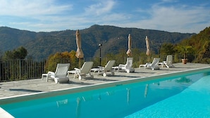 Piscina con sillones de playa y sombrillas, rodeada de un paisaje montañoso.