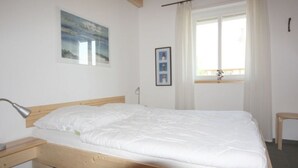 Un lit simple avec un cadre en bois, une table de chevet, une lampe, une fenêtre avec des rideaux et un tableau encadré au mur.