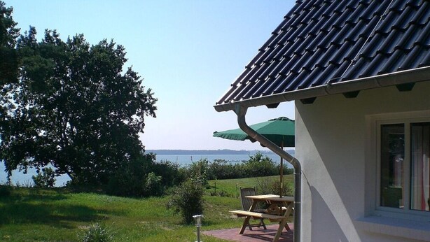 Une maison avec un toit en tuiles, un chemin en briques, une table de pique-nique et un parasol vert.