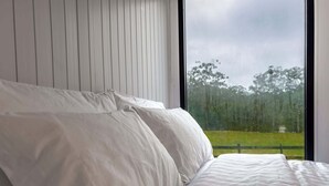 Ein Schlafzimmer mit großem Fenster, einem Bett mit weißer Bettwäsche und einem Holz-Kopfteil.