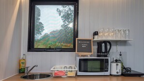 Eine kompakte Küche mit Spüle, Mikrowelle, Toaster, Wasserkocher und einem Fenster mit Blick auf Bäume.