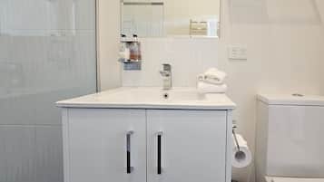 Ein Badezimmer mit einem weißen Waschbecken, Spiegel und WC. Unter dem Waschbecken befinden sich zwei Schränke, einer davon mit einem Handtuchhalter.