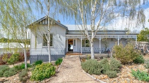 A two-story house with a front porch, a gravel pathway leading to the entrance, and a variety of shrubs and trees in the garden.