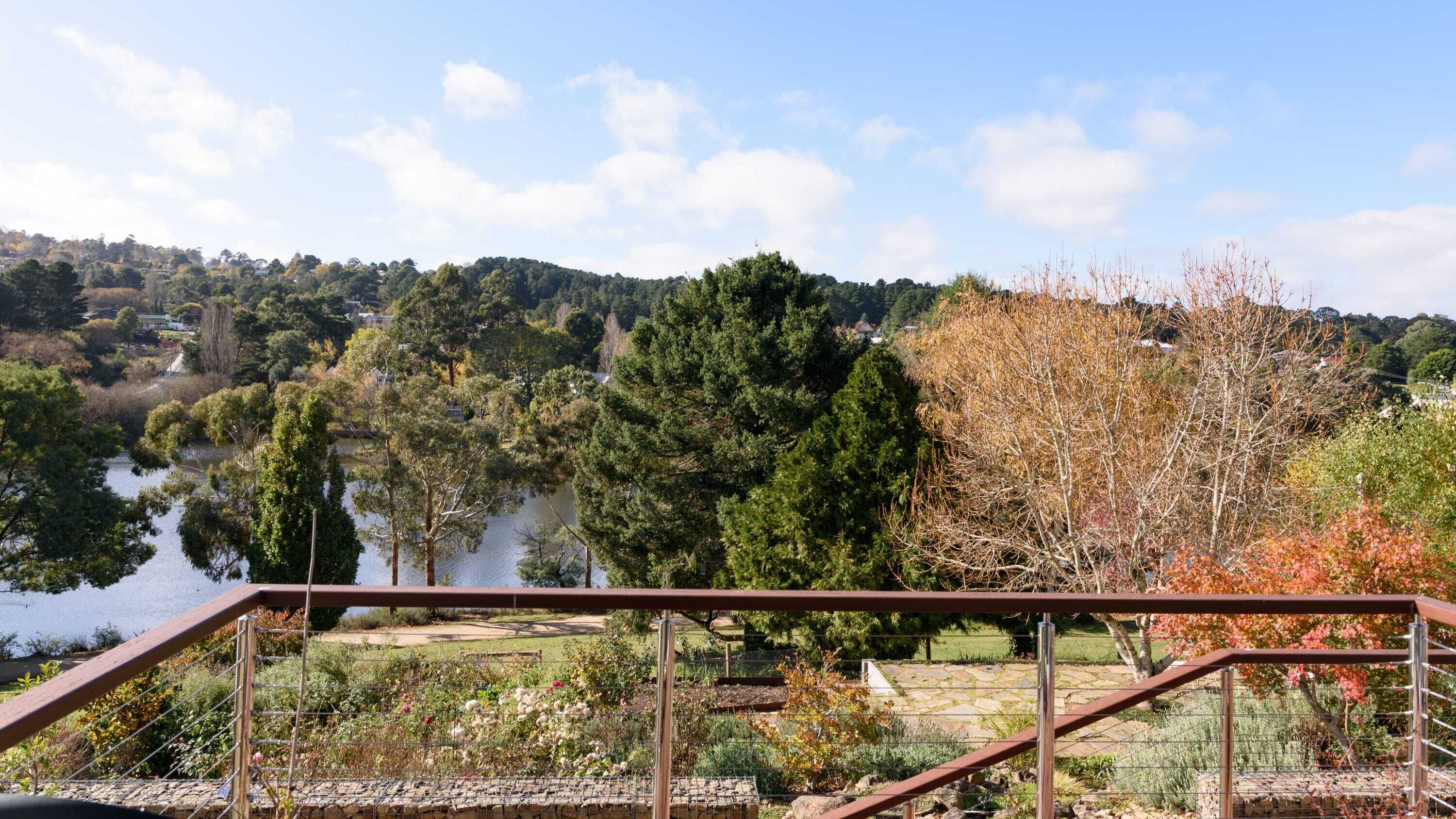 A scenic view from a balcony overlooking a lake, surrounded by trees and a hilly landscape.