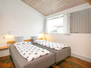 A room with two single beds, each with a pillow and a bedside lamp. There is a window with curtains, and the walls are white with horizontal lines. - 6 Person Holiday Home on a Holiday Park in Hanstholm (Hanstholm)