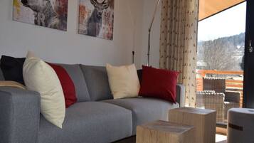 A modern living room with a grey sofa, red and white cushions, wooden side tables, and two deer-themed wall art pieces.