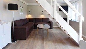 Een moderne woonkamer met een modulaire bank, een ronde salontafel en een trap met witte leuningen.