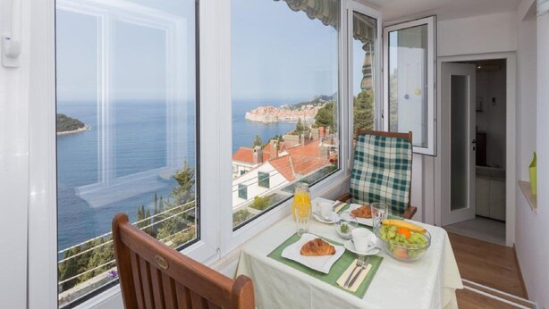 A balcony with a table set for breakfast, overlooking a coastal town and the sea. - Apartment Precious View (Dubrovnik)
