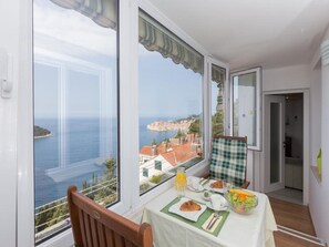 A balcony with a table set for breakfast, overlooking a coastal town and the sea.