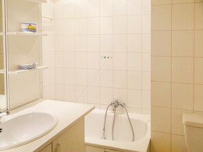 A bathroom with a white sink, a bathtub, and a mirror. There are shelves with decorative items on the wall. - Seaside Getaway w/ Balcony (Nieuwpoort)