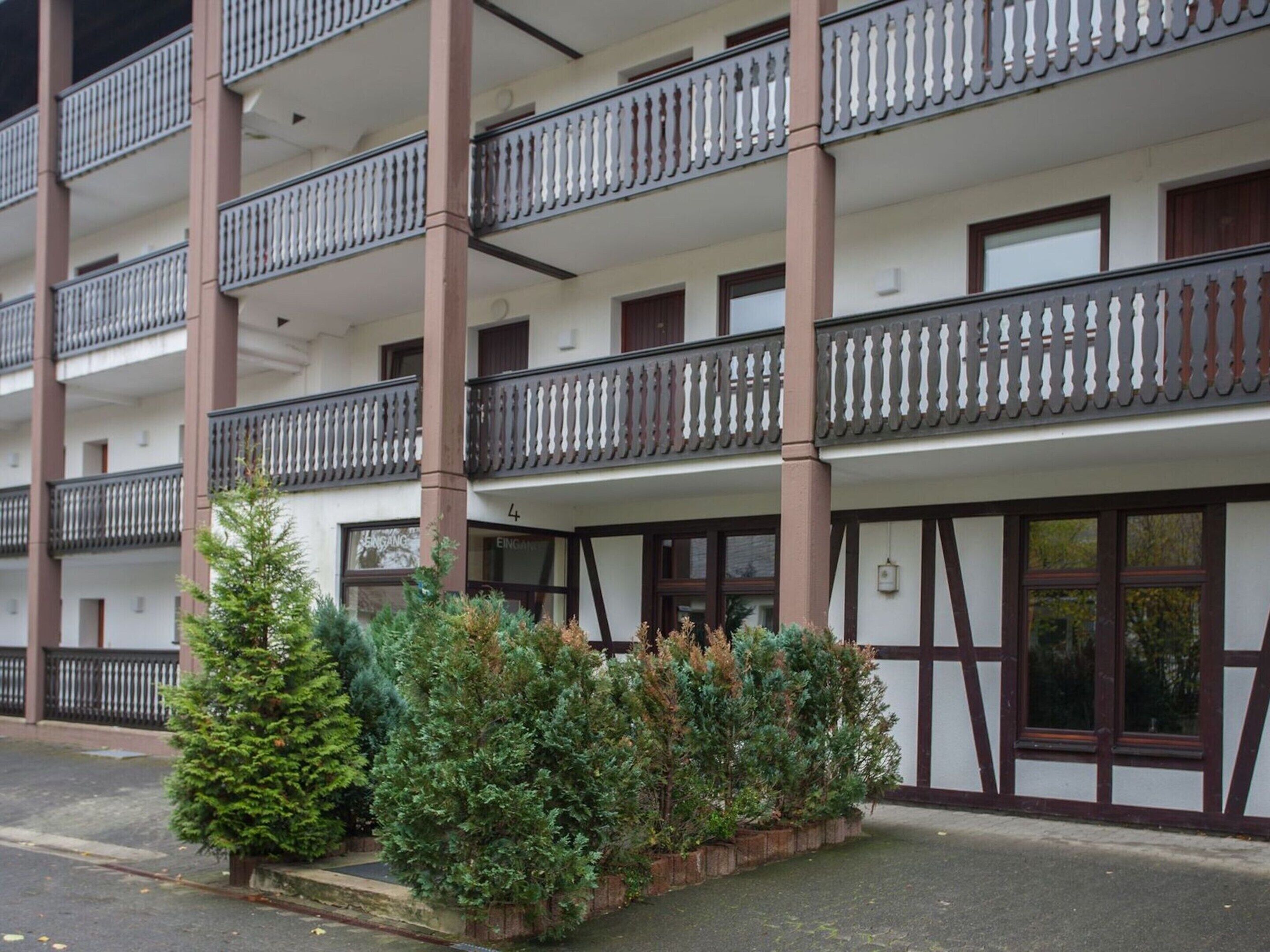 A multi-story building with balconies, a row of potted plants, and a traditional architectural style.