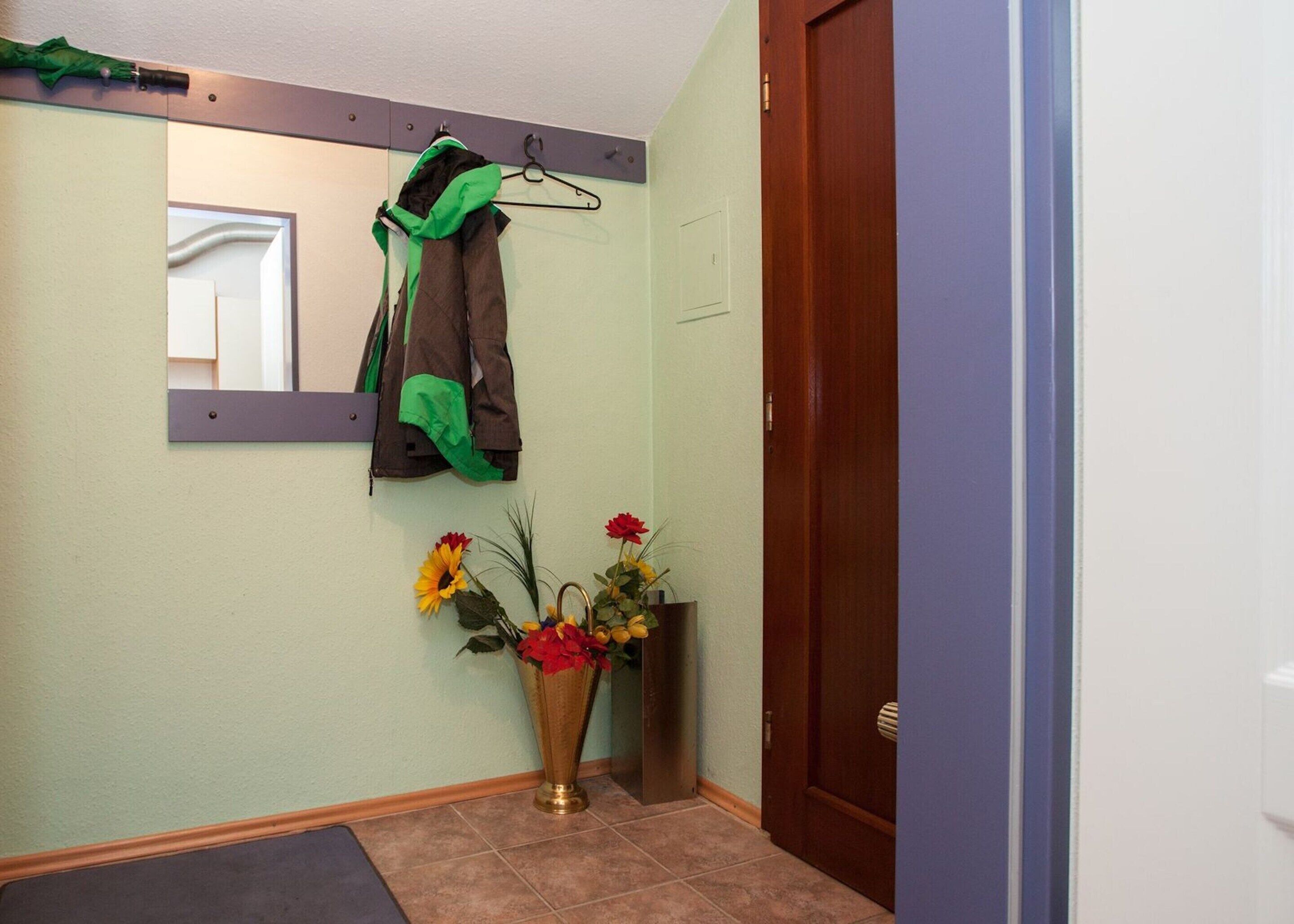 Ein Flur mit einem Garderobenschrank, der eine Jacke, einen Spiegel und eine Vase mit Blumen beherbergt.
