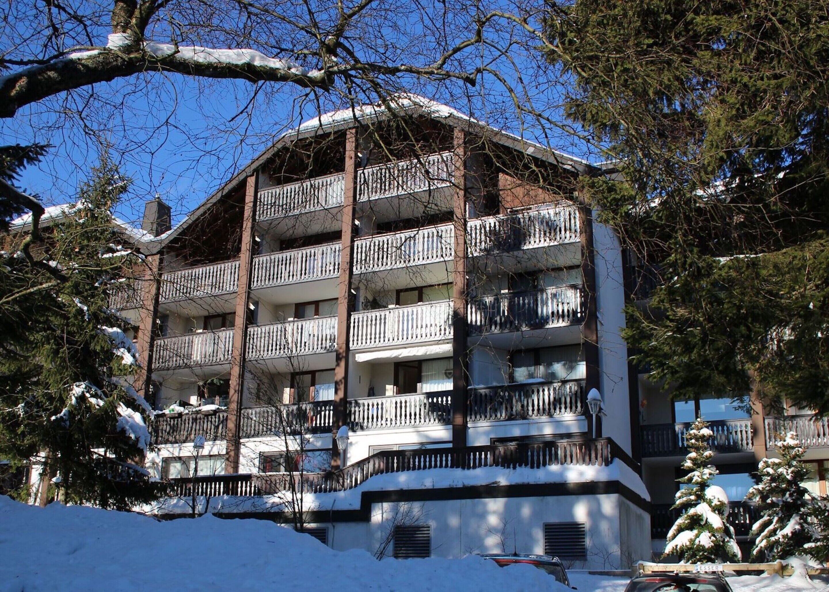 A multi-story building with balconies, surrounded by snow-covered trees.