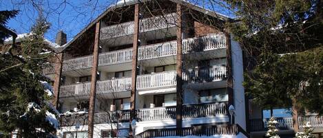 A multi-story building with balconies, surrounded by snow-covered trees.