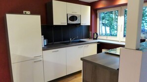 A compact kitchen with white cabinets, a microwave, and a window providing a view of trees. - Lovely Apartment in Neustadt (Neustadt am Ruebenberge)
