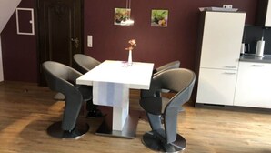 A dining area with a white table and four grey chairs, a dark wooden door, and a white cabinet with a small shelf. - Lovely Apartment in Neustadt (Neustadt am Ruebenberge)