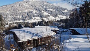 A wooden cabin with a snow-covered roof, surrounded by a snowy landscape and mountains in the background. - Grand Wastl Comfortable Holiday Residence (Woergl)
