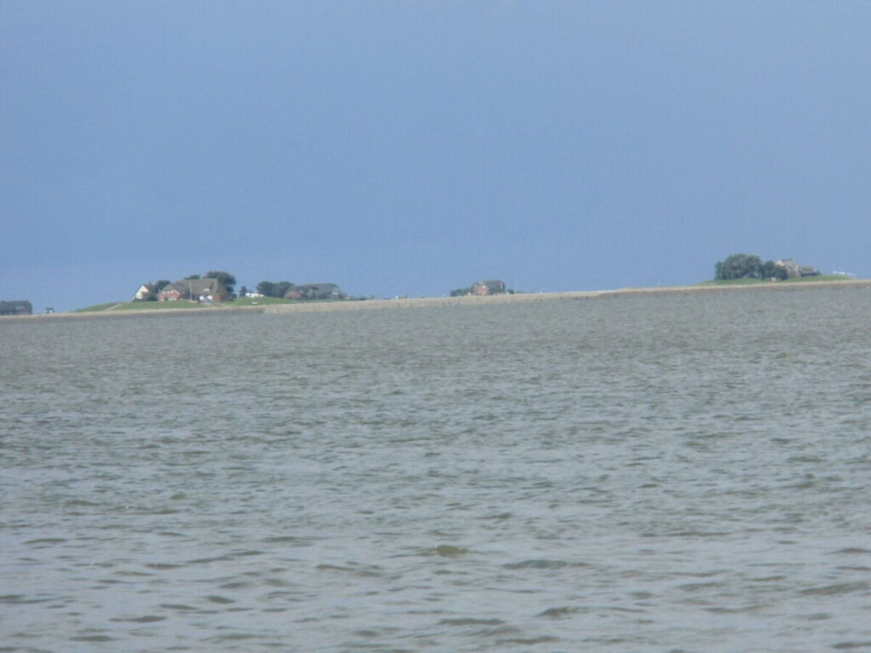 A coastal view with a sandy beach and a few buildings in the distance.