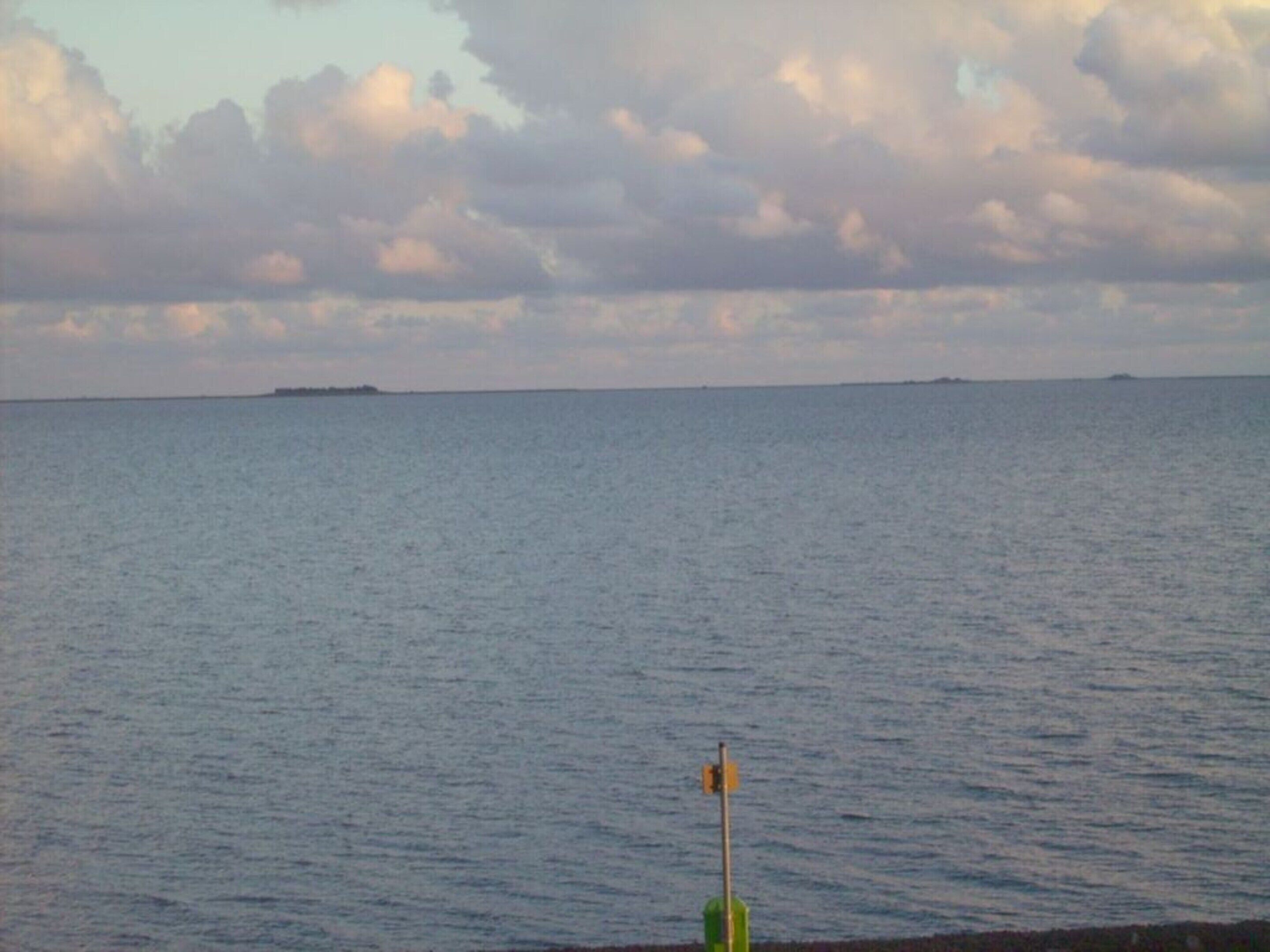 A calm sea with a distant island and a buoy in the foreground.