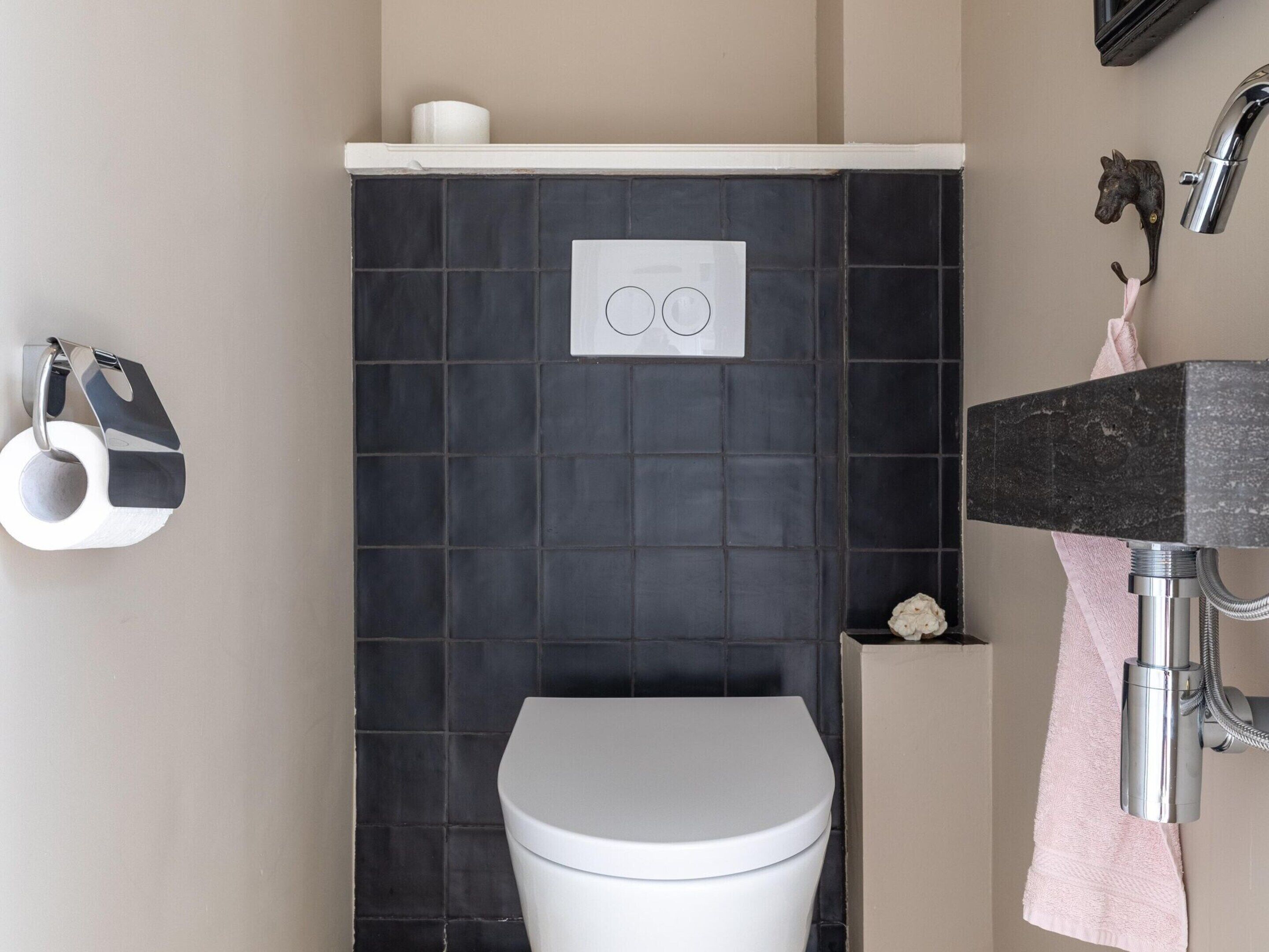 A bathroom with a white toilet, a black tiled wall, a sink with a marble countertop, and a towel hanging on the wall.
