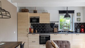 A modern kitchen with wooden cabinets, black tiled backsplash, and a dining area with a brown sofa. - Detached Retreat in Zoutelande Near Beaches (Zoutelande)