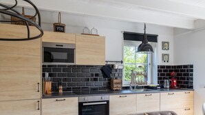 A modern kitchen with wooden cabinets, a black tiled backsplash, and a window with a view of greenery. - Detached Retreat in Zoutelande Near Beaches (Zoutelande)