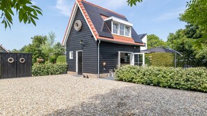 A black building with a red roof, a gravel driveway, and a hedge in front. - Detached Retreat in Zoutelande Near Beaches (Zoutelande)