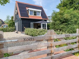 A house with a sloped roof, solar panels, and a wooden gate with "Koets" and "huys" signs.
