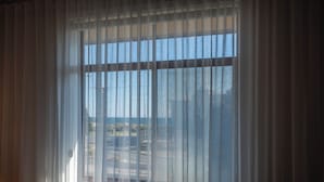 A room with a large window covered by sheer curtains, offering a view of the outdoors. - Cosy, fully-renovated apartment with ocean views and 1-minute walk to the beach (West Beach)