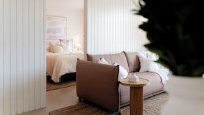A modern bedroom with a bed, a sofa, and a small side table. - Cosy, fully-renovated apartment with ocean views and 1-minute walk to the beach (West Beach)