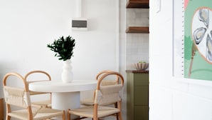 A dining area with a round white table, four woven chairs, and a potted plant. - Cosy, fully-renovated apartment with ocean views and 1-minute walk to the beach (West Beach)