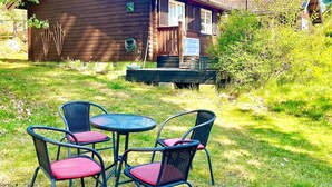 A wooden cabin with a deck, surrounded by grass and trees. - 5 Person Holiday Home in Gunnebo (Gunnebo)