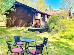 Une cabane en bois dotée d’une terrasse, entourée d’herbe et d’arbres.