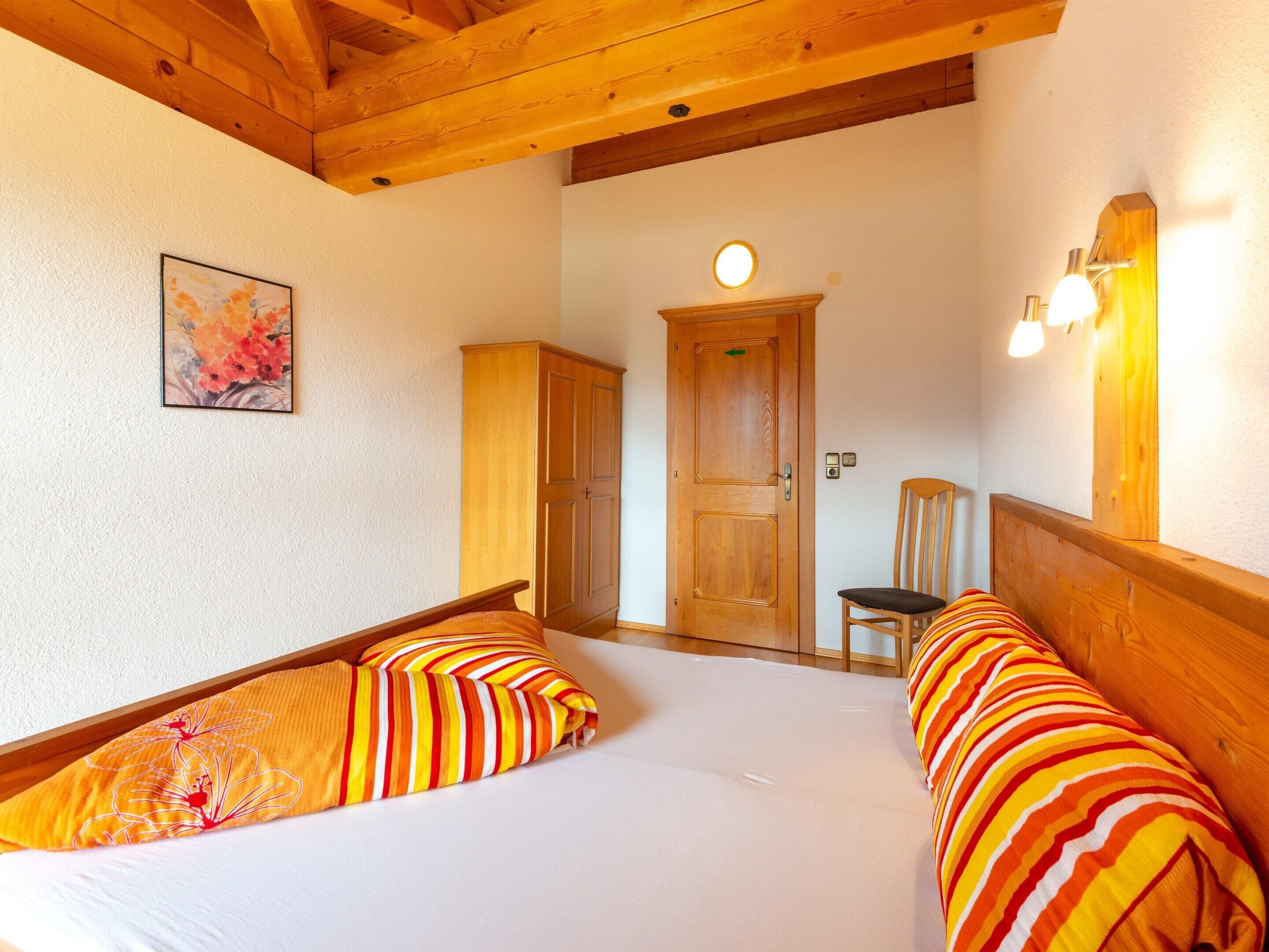 Une pièce avec deux lits, une armoire en bois, une porte, une chaise et un luminaire fixé au mur.