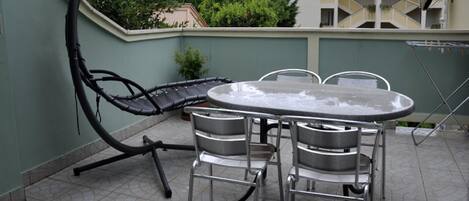 A patio with a round table and four chairs, a large umbrella, and a satellite dish on the building in the background.