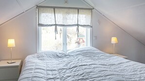 A bedroom with a bed, two bedside lamps, a window with curtains, and a sloped ceiling. - 6 Person Holiday Home in Fjallbacka (Fjallbacka)