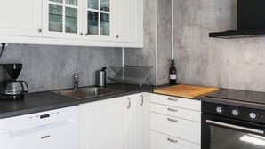 A modern kitchen with white cabinets, a built-in dishwasher, a coffee maker, a wine bottle, and a stove. - 6 Person Holiday Home in Fjallbacka (Fjallbacka)