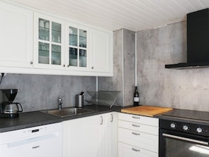 A modern kitchen with white cabinets, a built-in dishwasher, a coffee maker, a wine bottle, and a stove. - 6 Person Holiday Home in Fjallbacka (Fjallbacka)