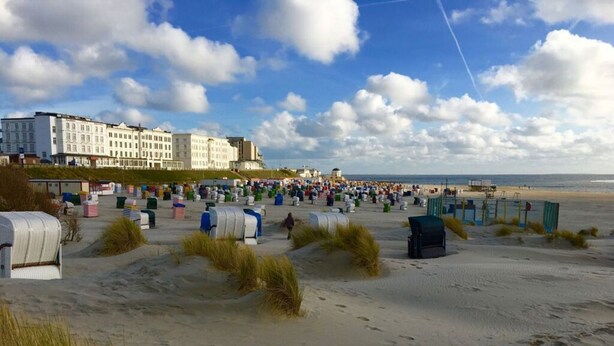 A beach with beach huts and a row of white buildings in the background.