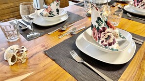 A dining table set with plates, glasses, and cutlery, with a view of greenery outside.