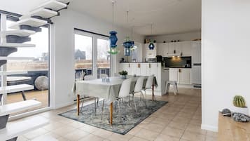 A modern kitchen with white cabinets, a dining area with a table and chairs, and a staircase leading to an outdoor deck.