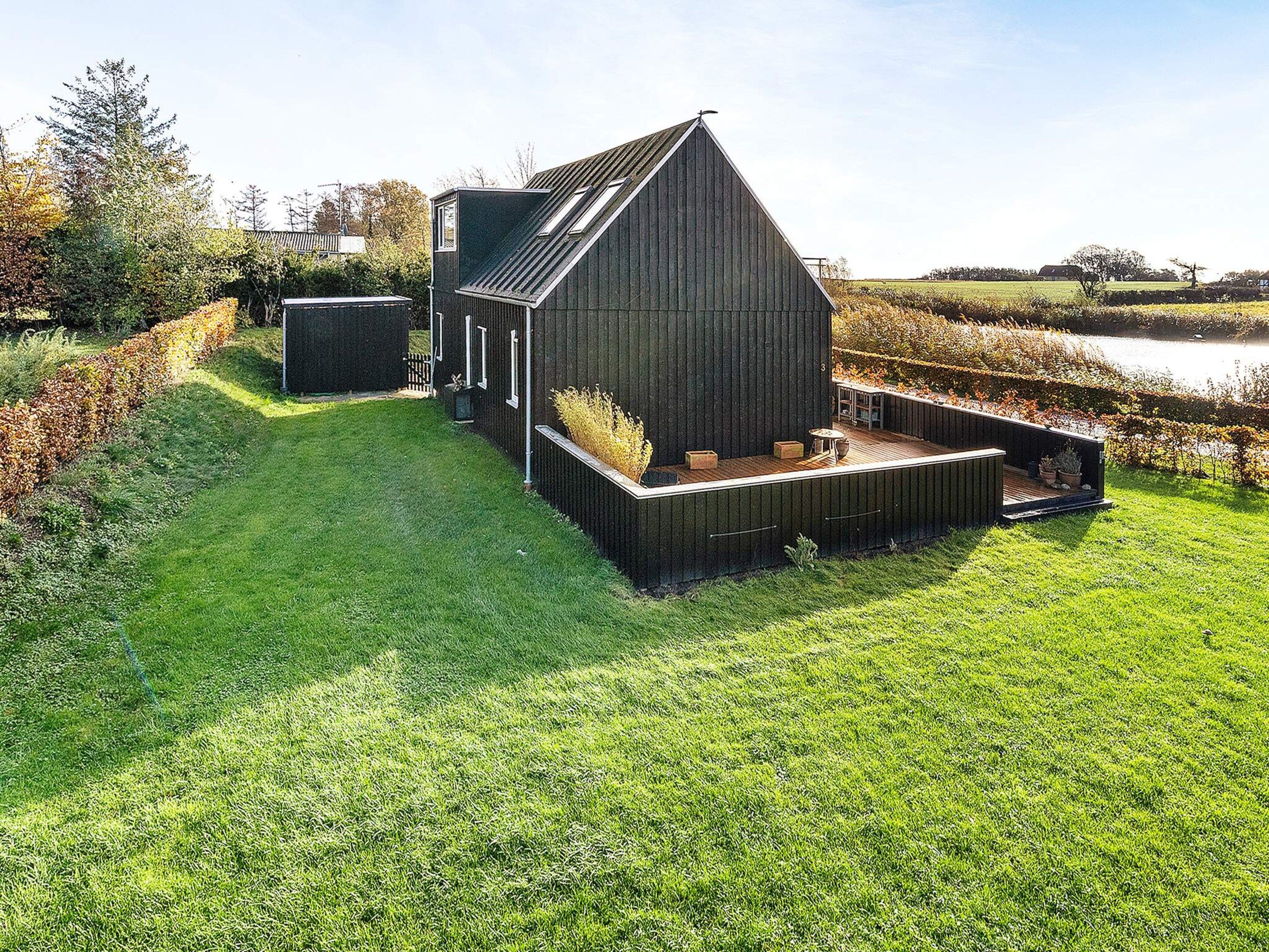 A modern barn-style building with a sloped roof, a deck area with seating, and a surrounding grassy landscape.
