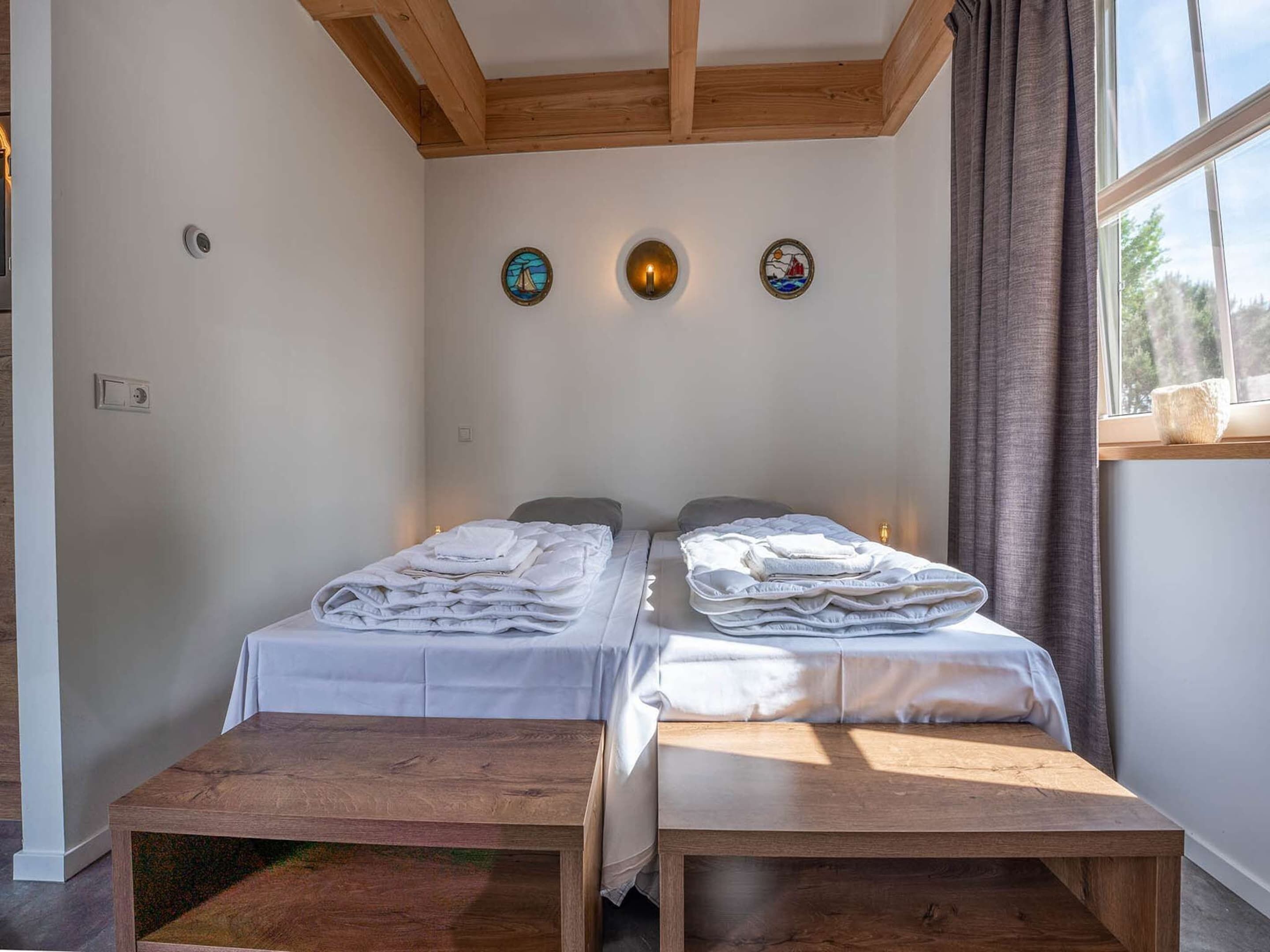 Ein Zimmer mit zwei Betten, einer hölzernen Sitzbank und einem Fenster mit Vorhängen.