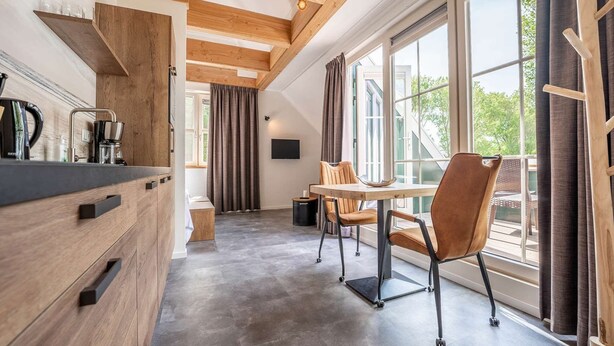 Una cocina moderna con vigas de madera, un comedor con mesa y sillas, y ventanas amplias con vistas al exterior.