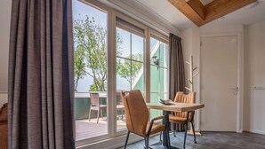 Una habitación moderna con un amplio ventanal corredera que da a un espacio exterior, techo de madera y una pequeña mesa con sillas.