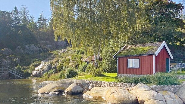 A red wooden cabin by a lake with a stone wall and a wooden dock. - 7 Person Holiday Home in Tjorn-by Traum (Myggenäs)